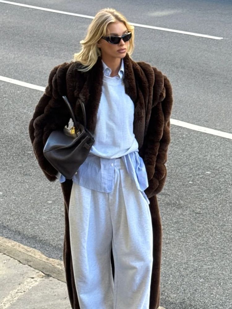 Elsa Hosk wears light grey sweatpants with a blur striped shirt layered under a white sweatshirt and a brown vintage fur coat