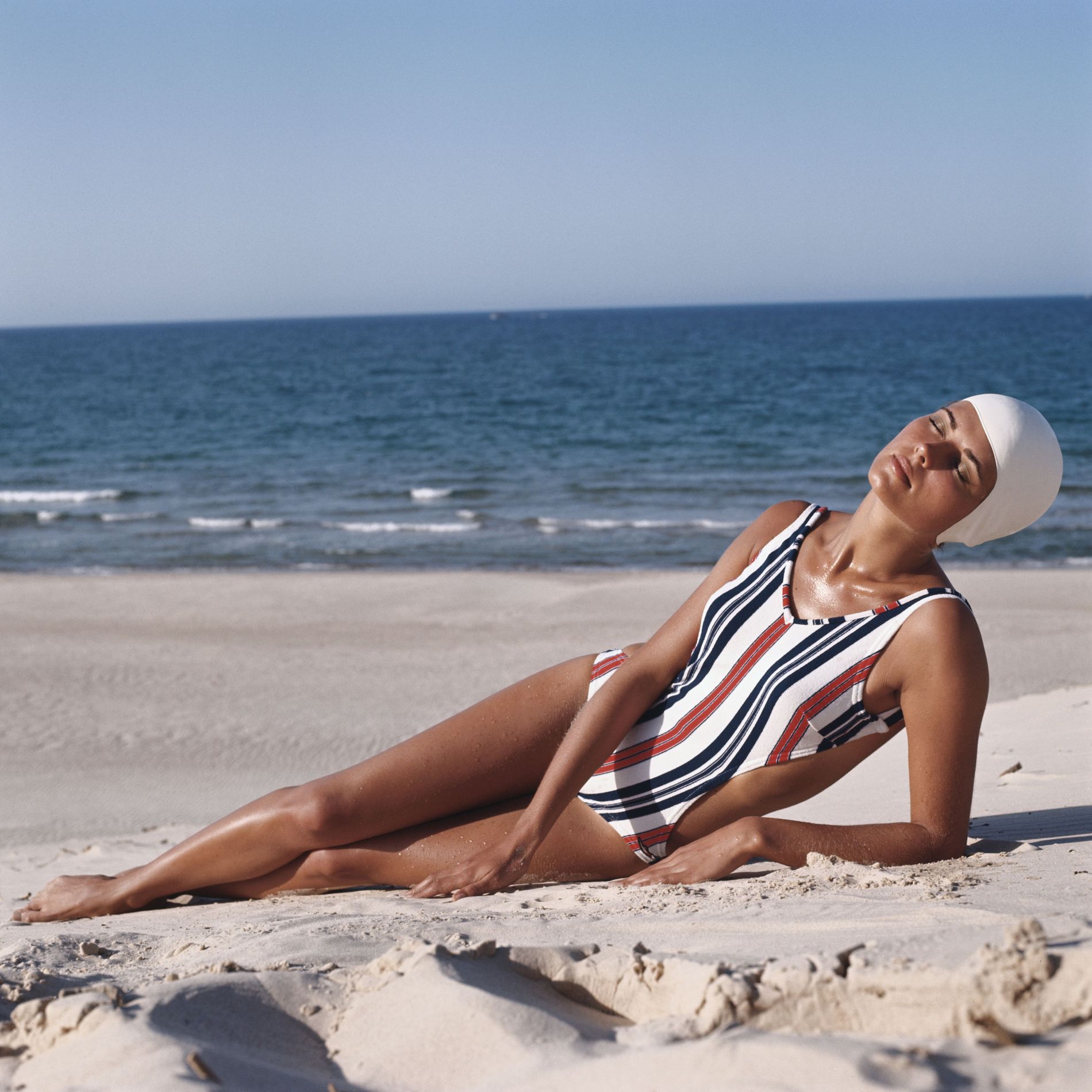 Model on beach wearing striped swimwear