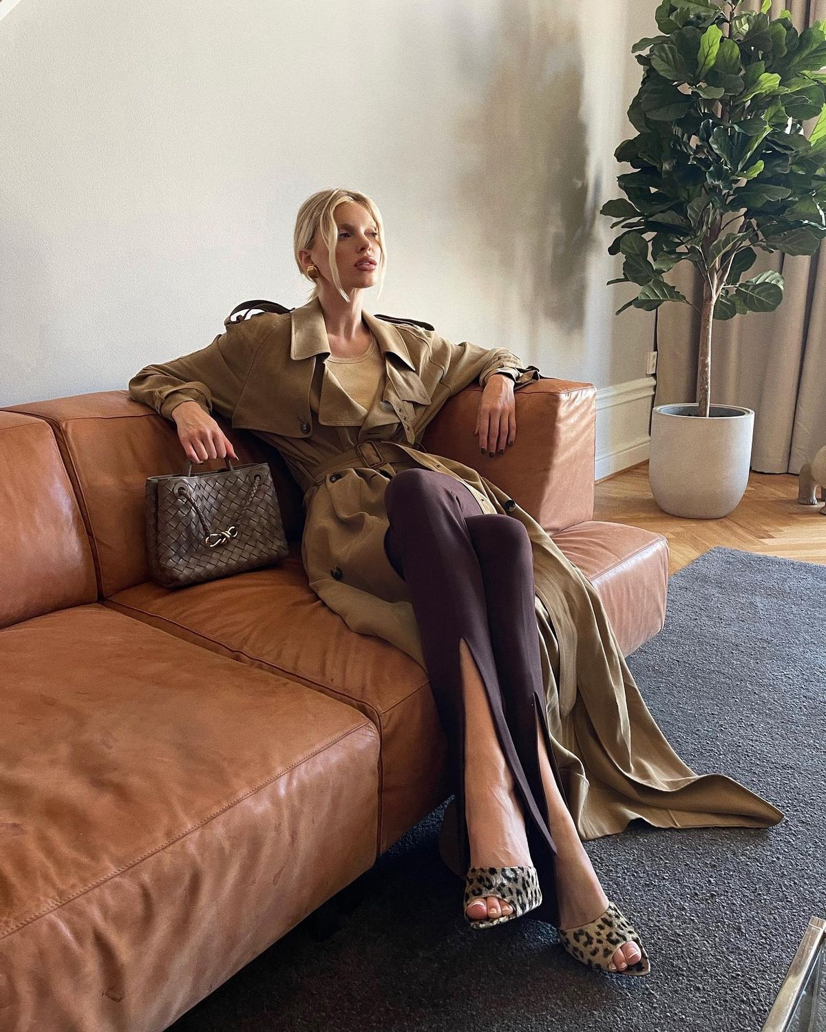 Elsa Hosk wears double-breasted trench coat by Saint Laurent, clip-on vintage earrings by Saint Laurent, and stretchy brown The Attico trousers.