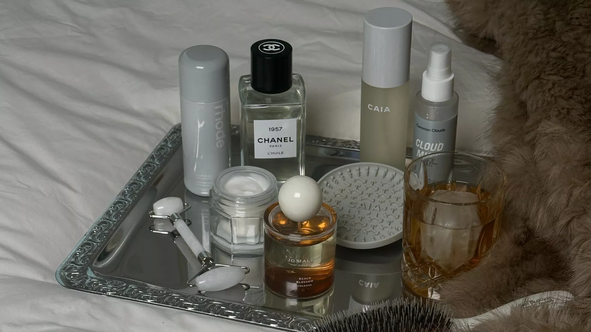 A collection of beauty items upon a silver tray on white sheets 
