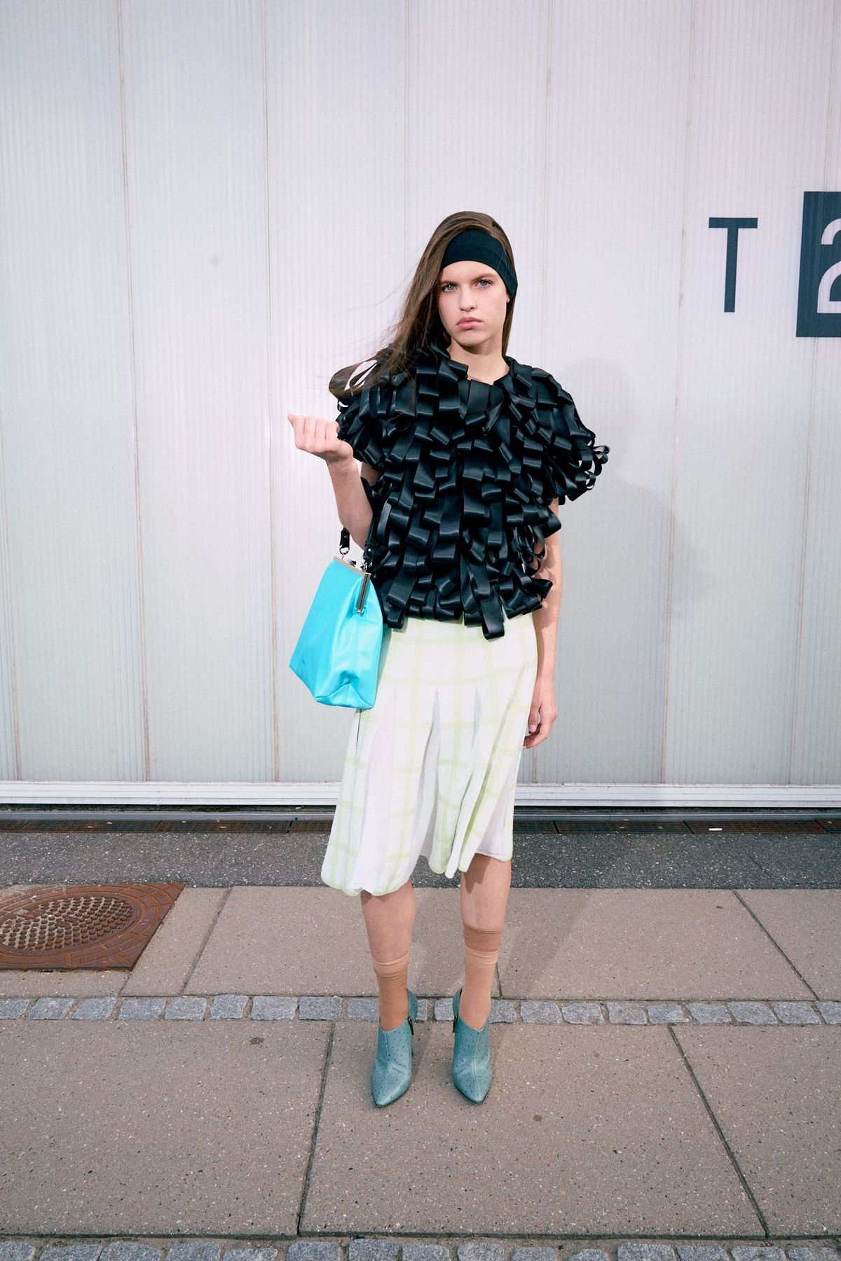 A model walking the Nicklas Skovgaard SS27 runway show carries a teal clasp-closure handbag, created in collaboration with Hvisk