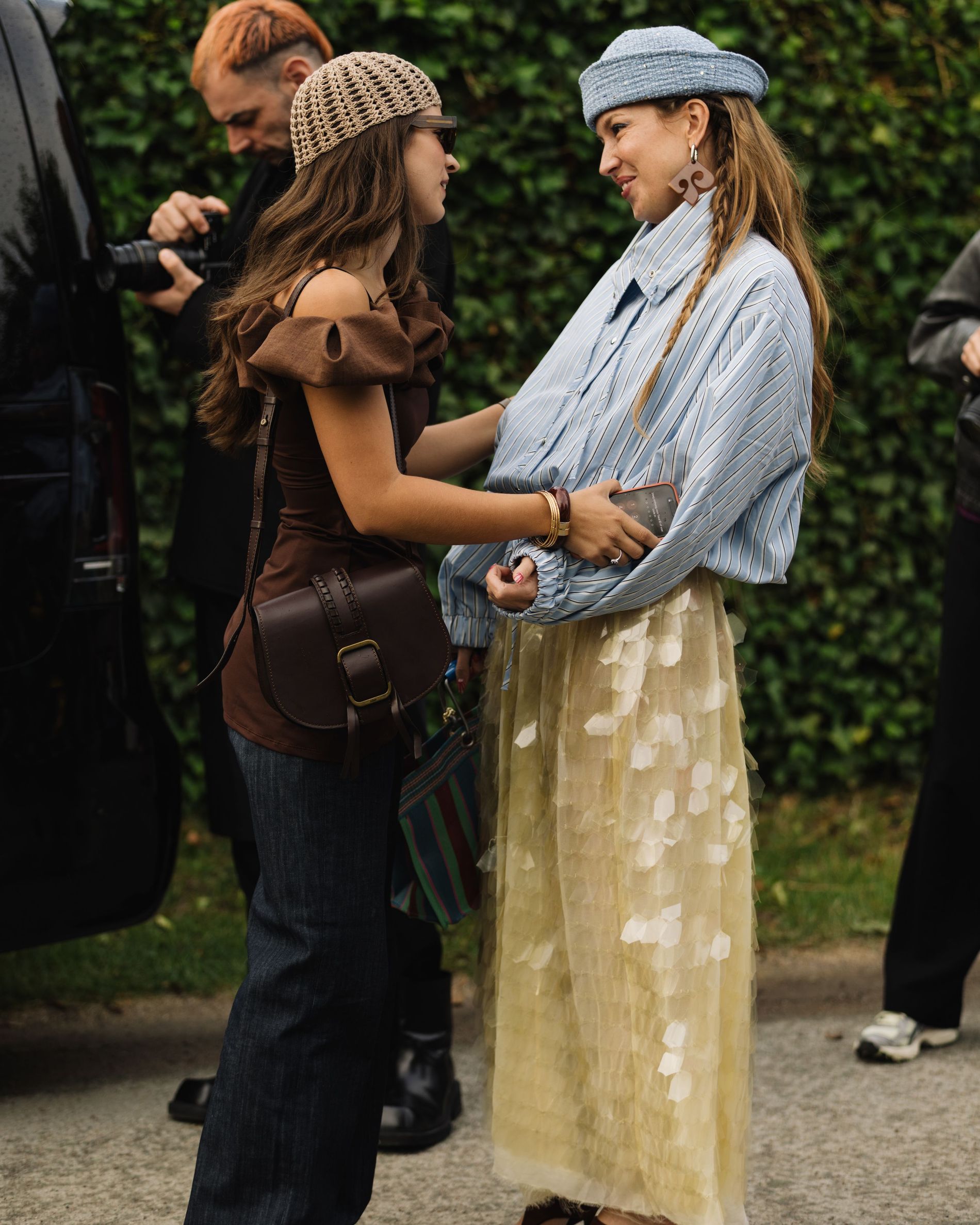 Streetstyle images of the women hugging each other, wearing a yellow sequin skirt, a blue striped shirt and a blue denim hat  