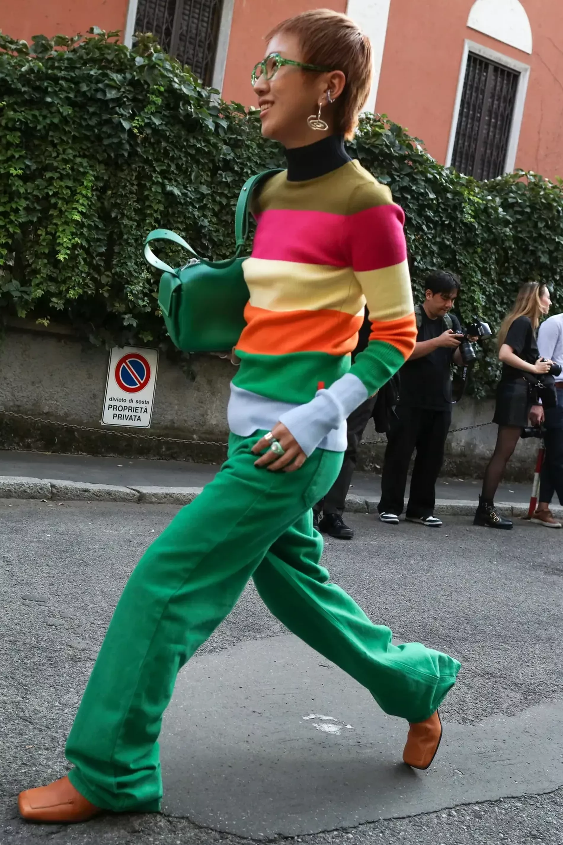 Milan fashion week guest wears vibrant striped turtleneck with green pants and brown boots 