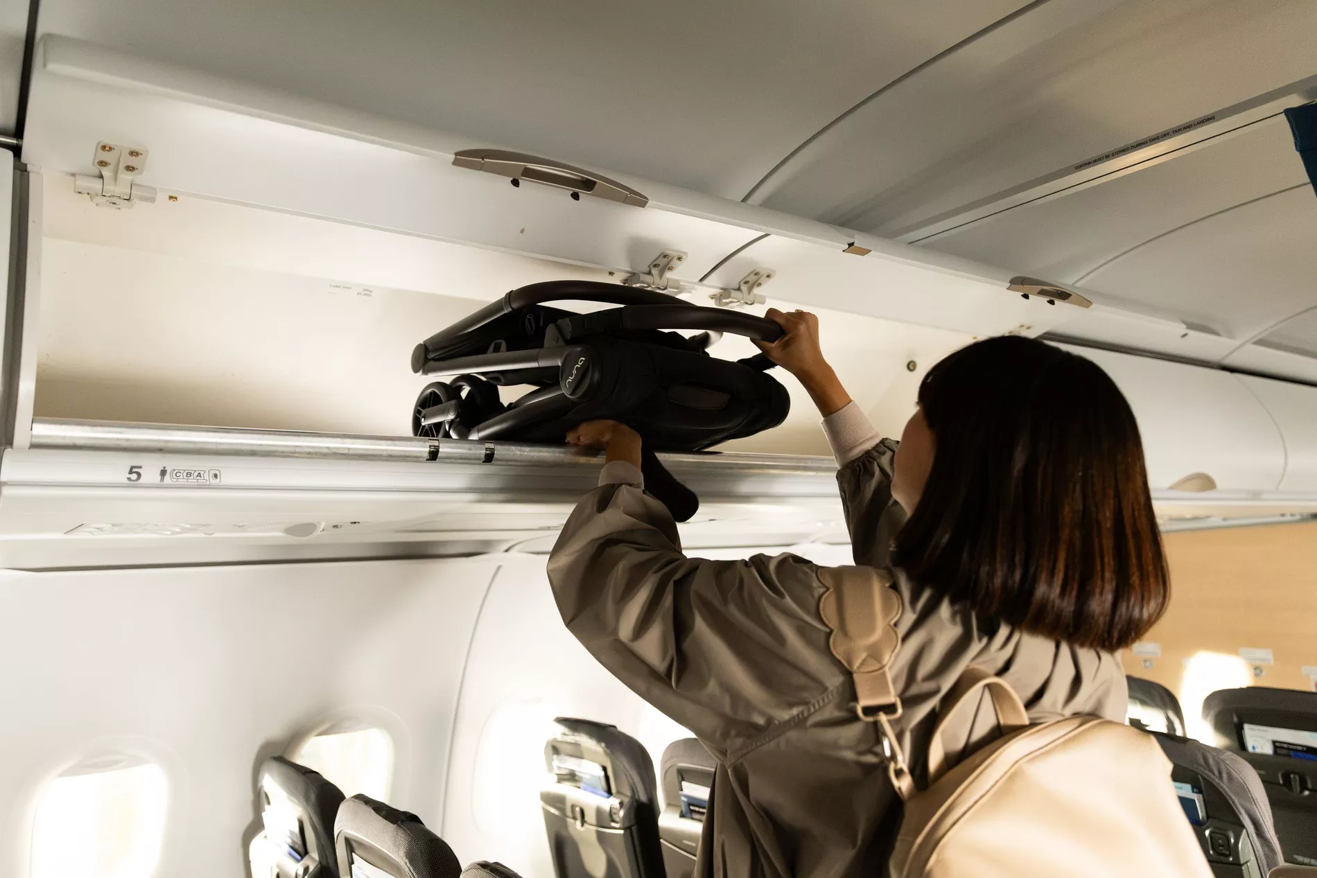 A woman places the folded down Nuna VIAA cabn into an overhead luggage compartment on a plane