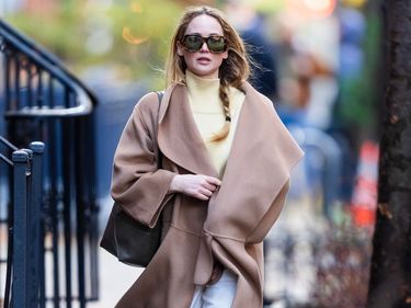 Actor Jennifer Lawrence wears a beige Toteme coat, a yellow turtleneck, white jeans and sneakers