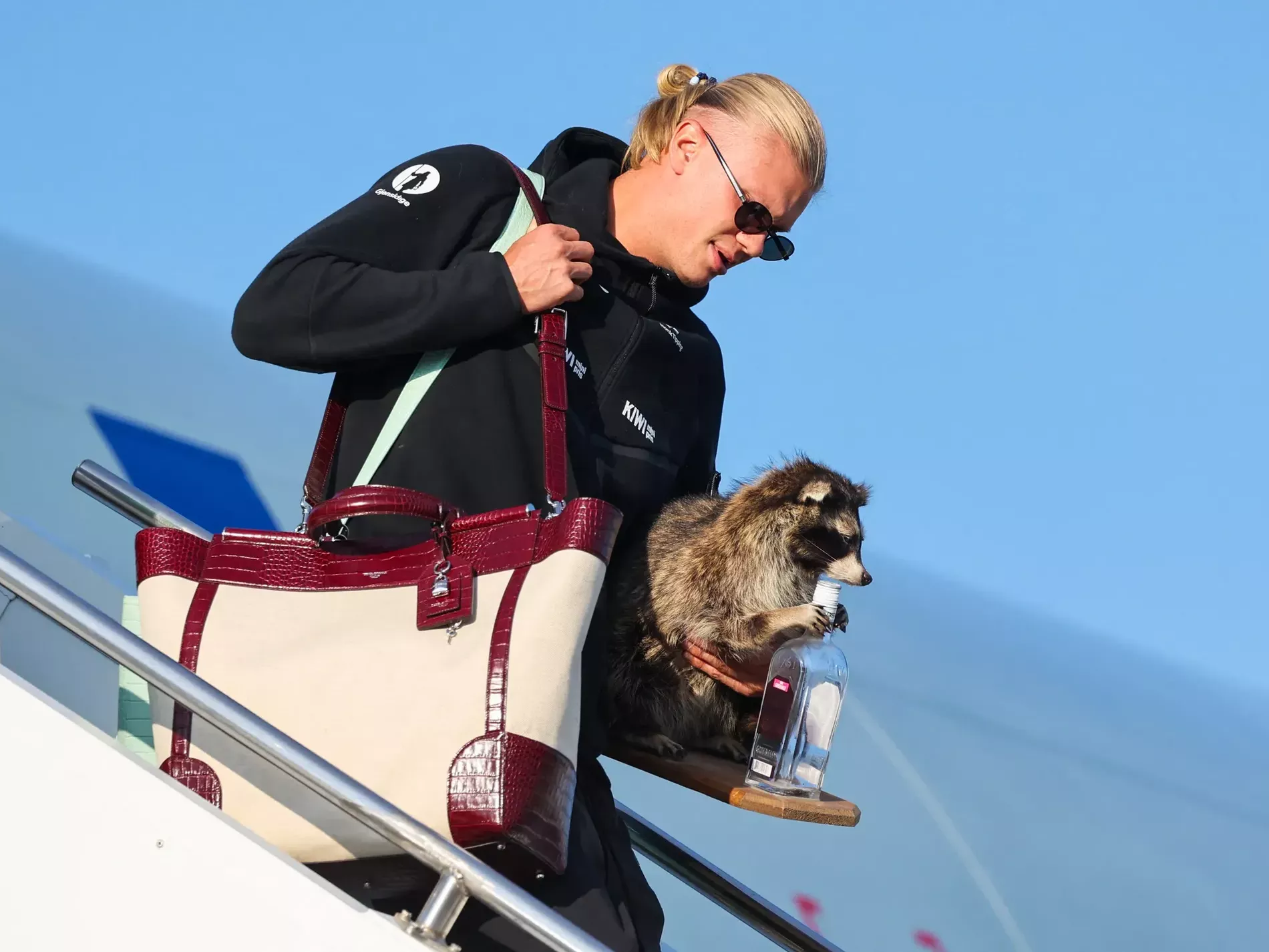 Erling Haaland stepping out of the plane in sunglasses wearing a big Dolce & Gabbana Sicily Tote Bag and holding a racoon in his left hand