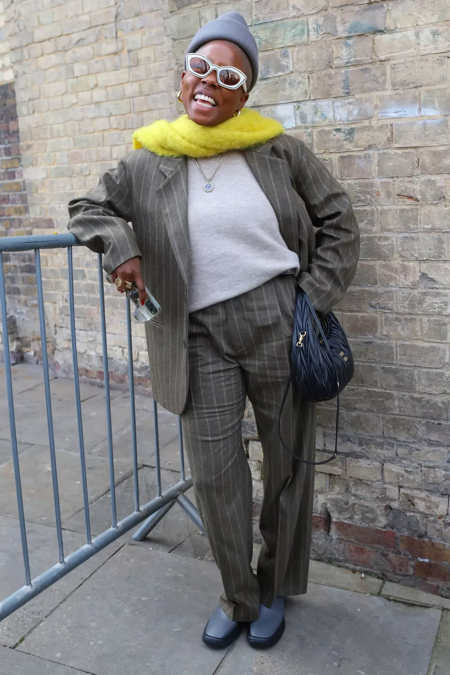London Fashion Week Guest wears greige pinstripe suit with grey sweater and bright yellow scarf 