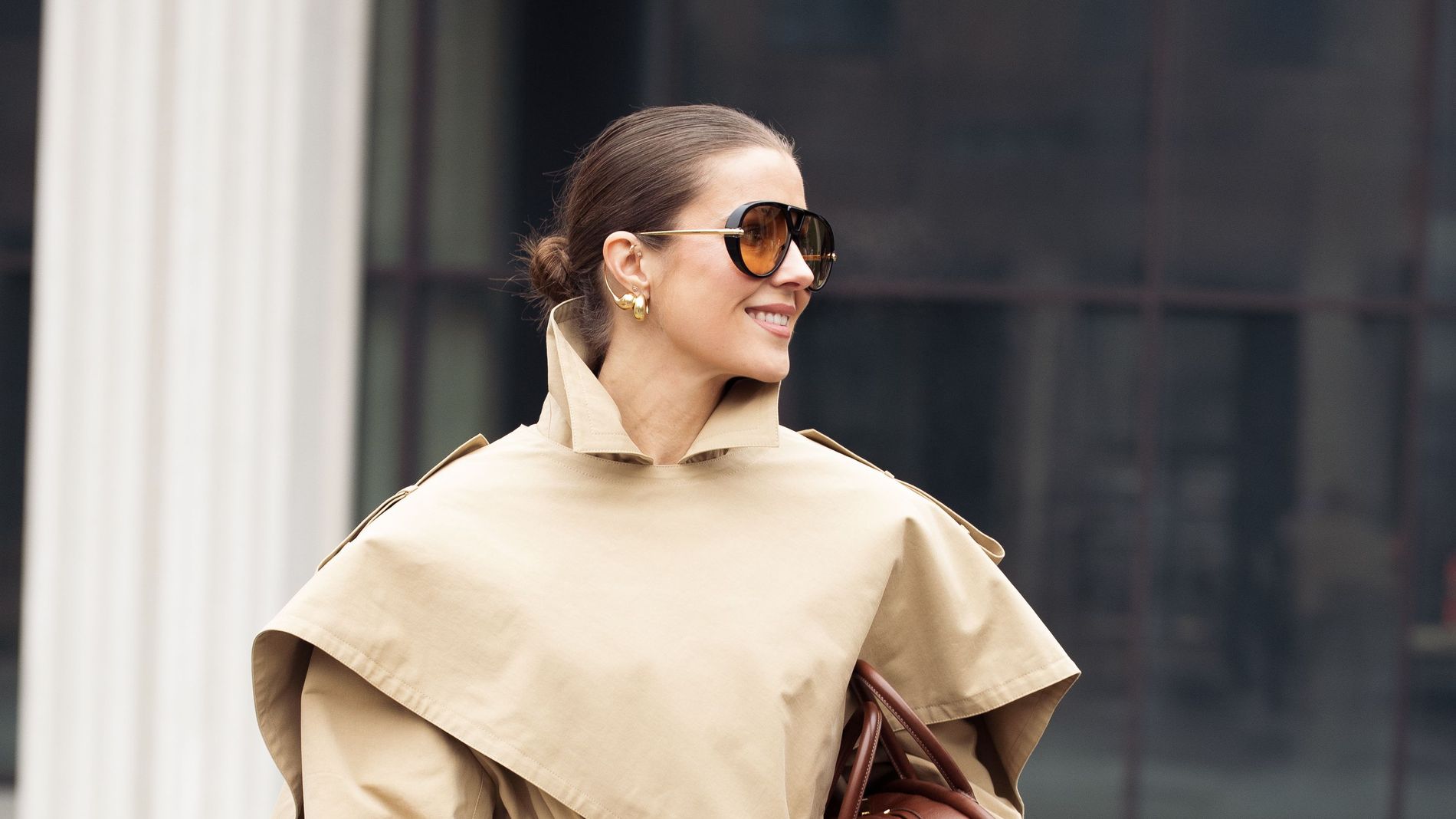 Nina Sandbech wears her hair slicked back into a bun, paired with sunglasses, a trenchcoat and a brown bag