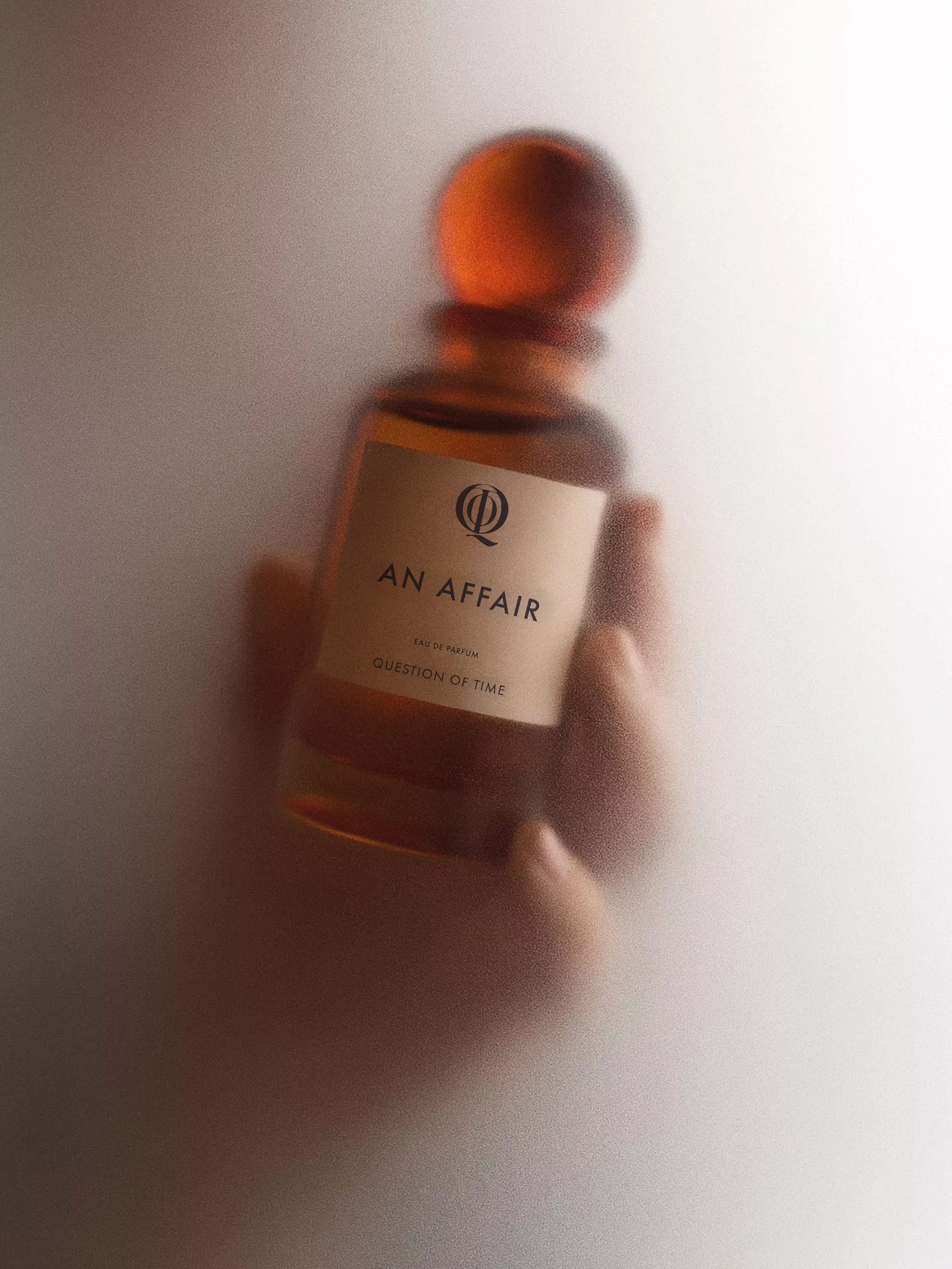 QOT's perfume 'An Affair' held in hand and surrounded by steam