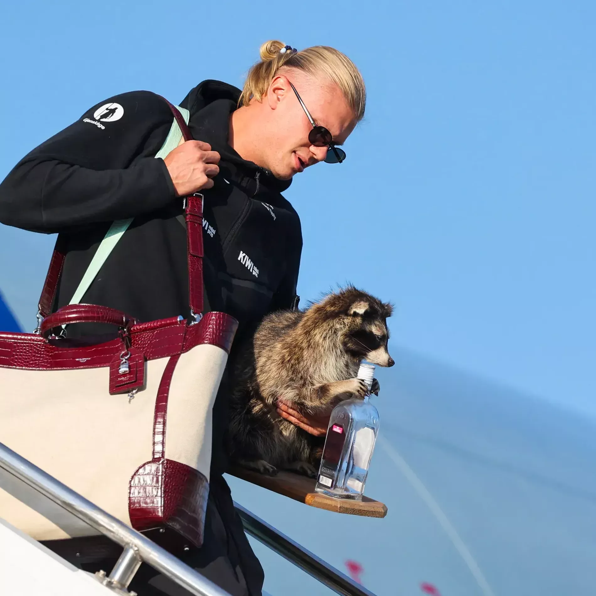 Erling Haaland stepping out of the plane in sunglasses wearing a big Dolce & Gabbana Sicily Tote Bag and holding a racoon in his left hand