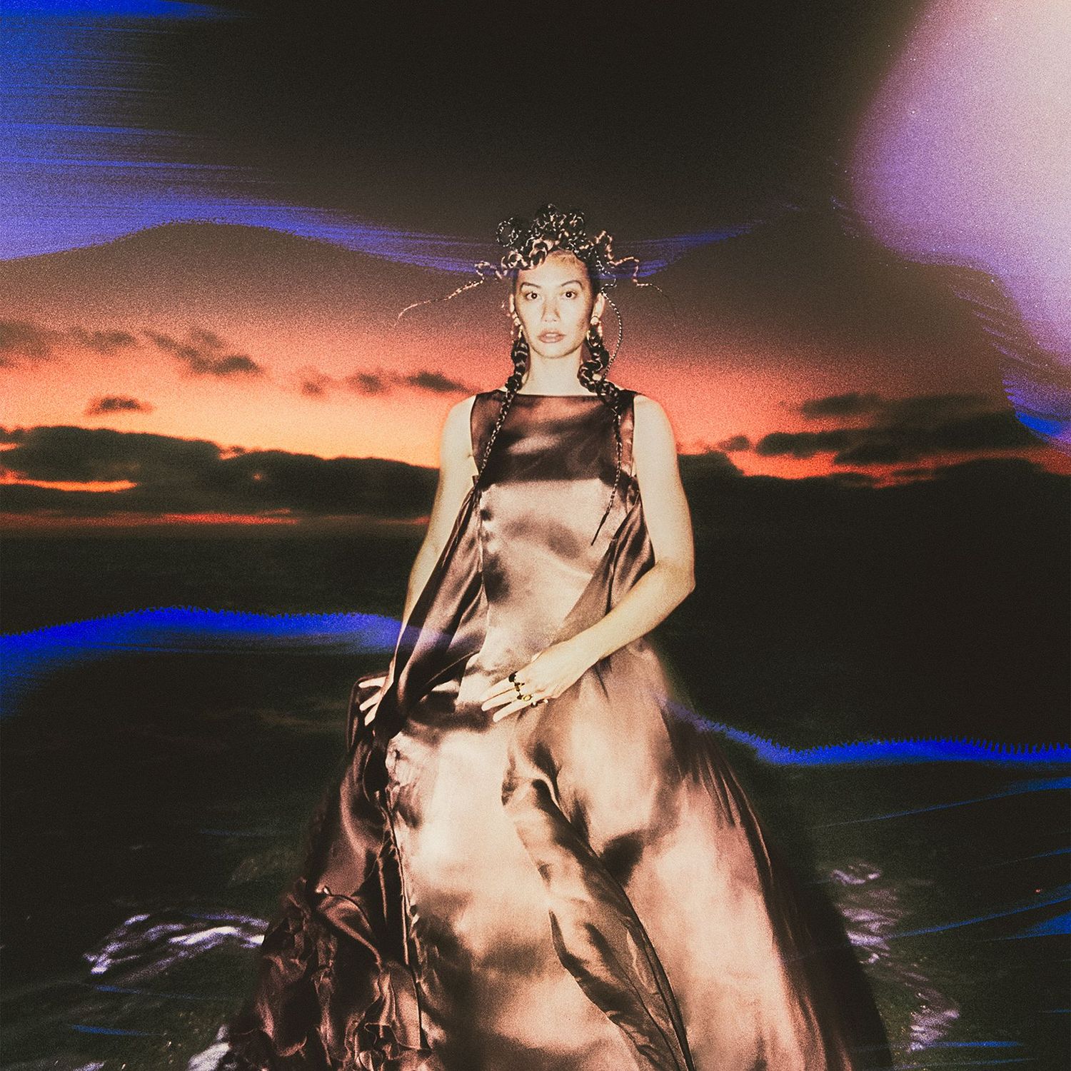 Model in satin dress stands outside with aurora above her