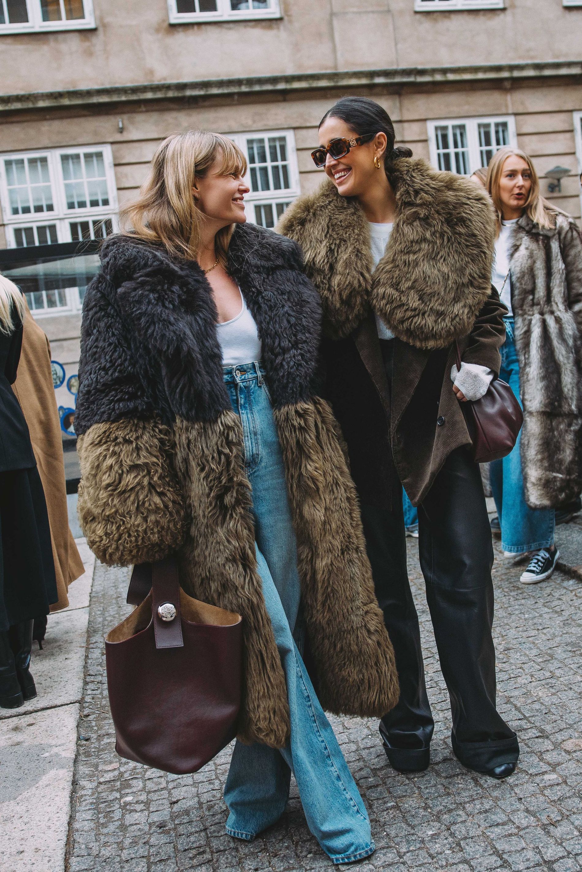 Jeanette Madsen and Darja Barannik wear faux fur coats paired with laid-back denim and brown leather handbags