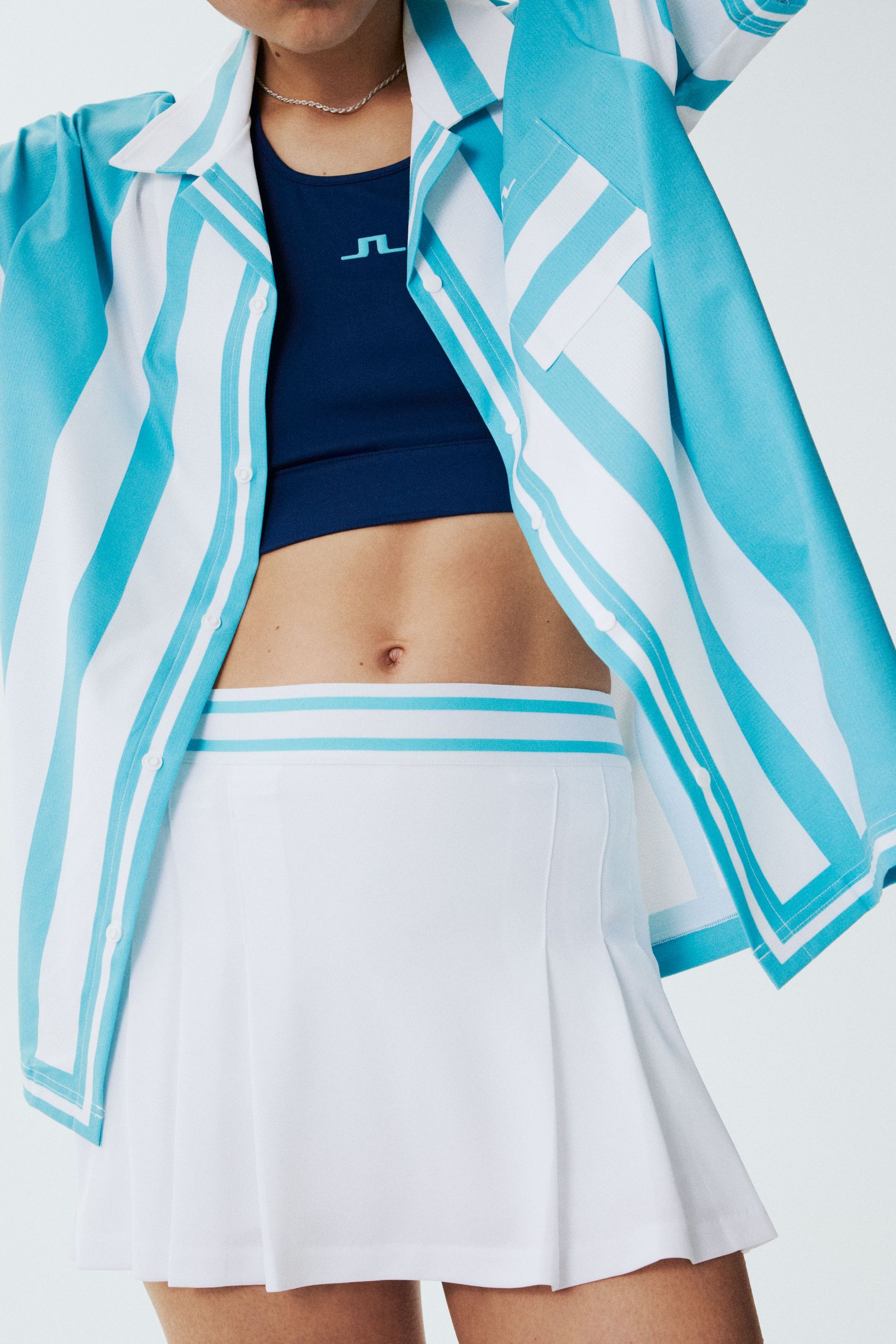 J.Lindeberg 2024 tennis collection - Pleated white tennis skirt with a navy bralet and a patterned teal polo shirt