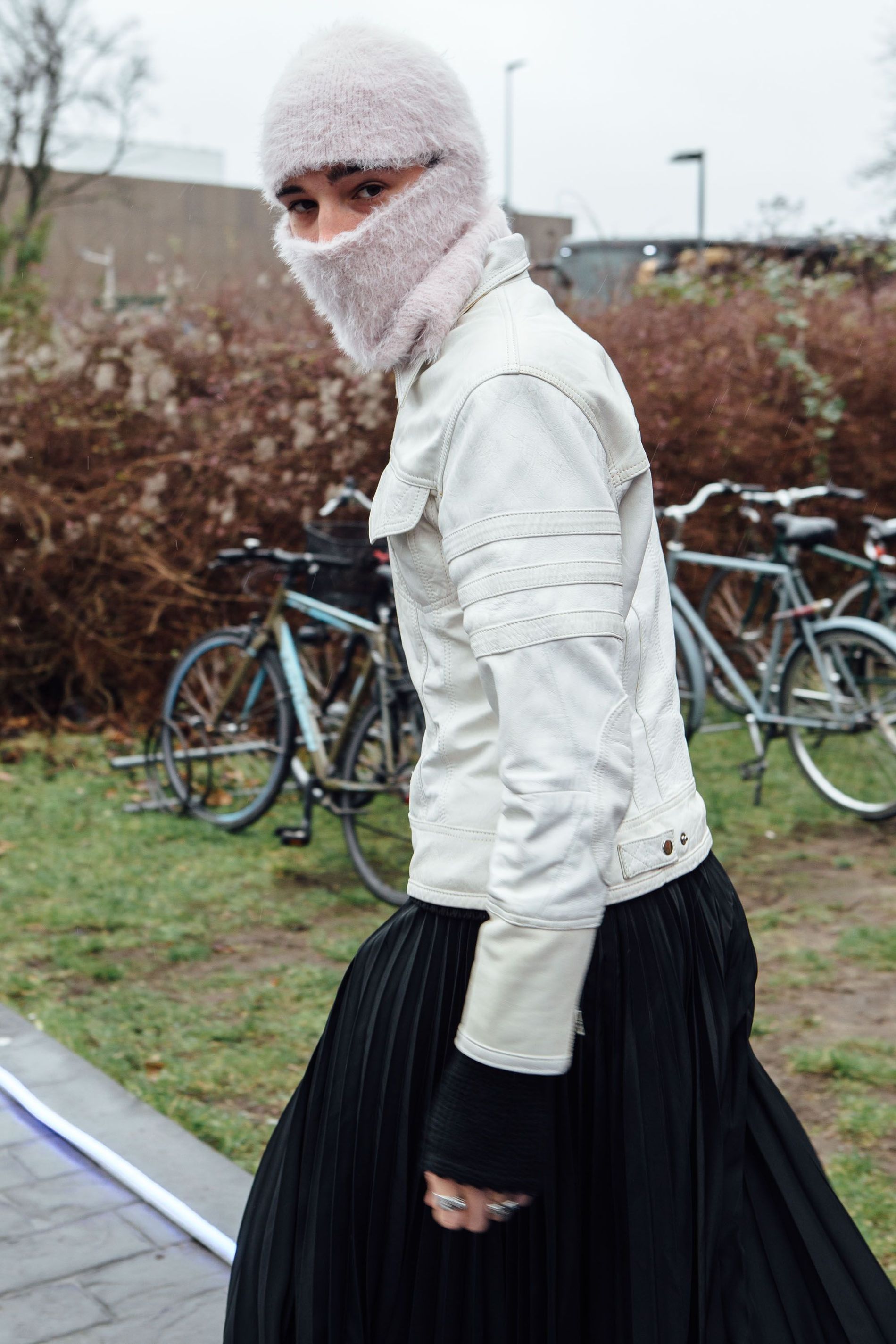 A guest wears a fuzzy pale pink balaclava with a white leather jacket and black pleated skirt