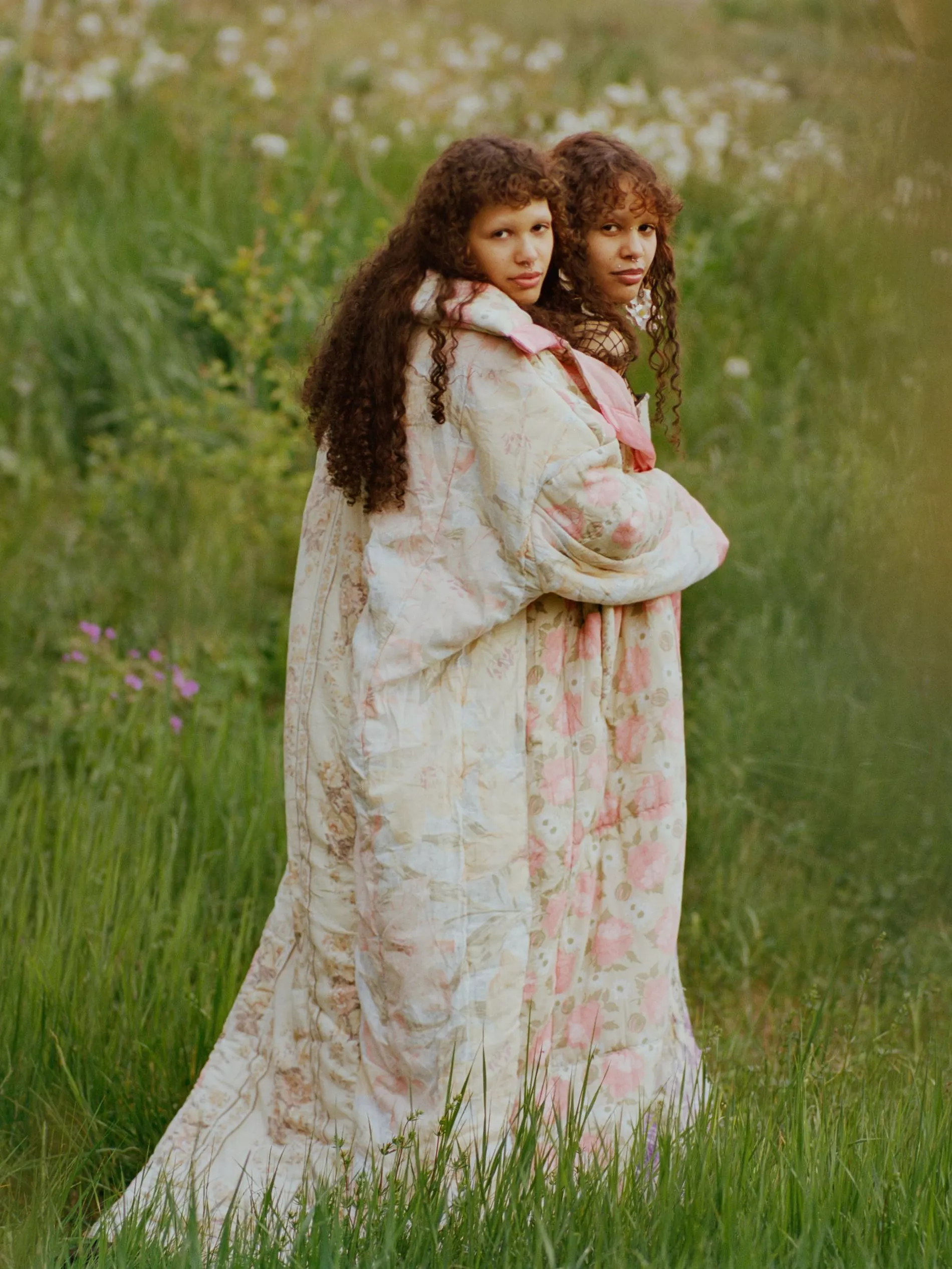 Two models stand in a field wearing quilted rose-printed long coats