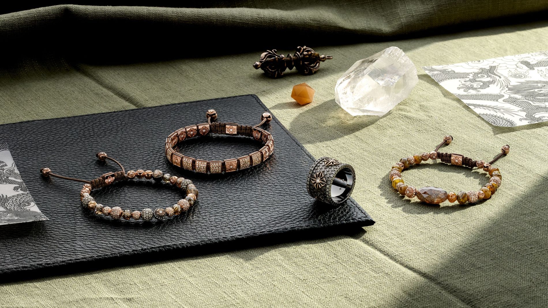 These are Shamballa Jewels luxury macramé-braided bead bracelets and a ring, crafted in 18k gold with precious gemstones and pavé-set diamonds on a green linen cloth
