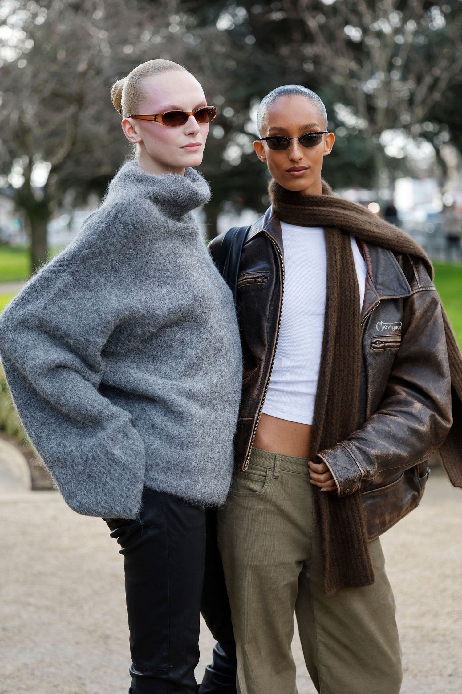 Alex Consani wears grey sweater, black pants (L), and Mona Tougaard wears white t-shirt, brown leather jacket, brown scarf, black bag, olive green pants