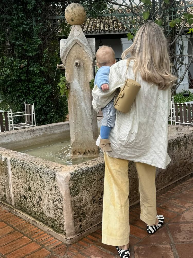 Josefine HJ with her kid outside with a oversized striped shirt paired with yellow manchester trousers, and a chanel bag and khaite zebra slides